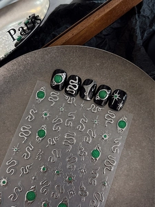 Macro shot of 3D embossed emerald snake and star metallic nail art stickers on black tips