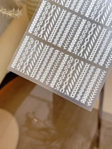 Macro detail of 3D embossed nail stickers featuring white knitted sweater textures