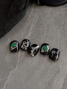 Detail of gothic black press-on nails with silver snake relief and green gemstone