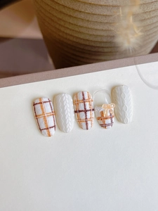 Detailed view of 3D knit texture nail stickers with orange plaid and ribbon bow