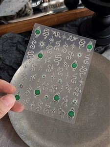 Macro detail of 3D emerald green snake nail stickers with silver glitter and evil eye motifs