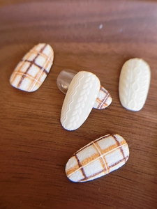 Macro view of 3D knit texture nail art stickers in cream and orange plaid on wood