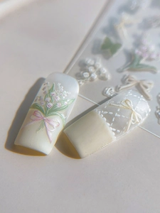 Detailed macro shot of 3D embossed lily of the valley and white lace bow nail stickers
