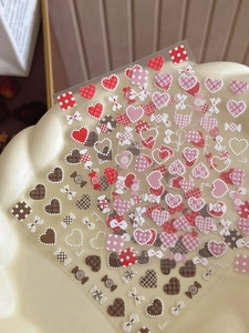 Detail of 3D embossed nail stickers with heart, candy, and bow designs in warm tones