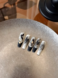 Dettaglio macro di unghie finte dipinte a mano con farfalle e accenti in foglia d'oro