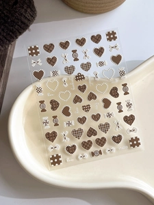 Detail showing 3D embossed heart and bow nail art stickers in cream and brown on a tray