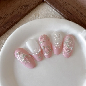 Pink embossed floral nail stickers with white bows and pearl accents on ceramic plate
