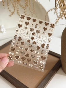 Macro detail of brown 3D bow and heart nail stickers with vintage checkerboard patterns