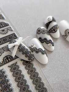 Detail of black lace nail art stickers and 3D ribbon bows on white press-on nails