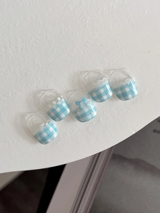 Detailed view of blue gingham nail tips with white lace patterns and 3D bow decoration