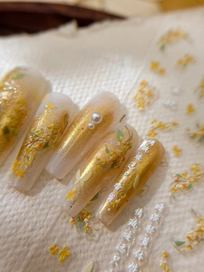 Macro detail of long coffin nails with gold foil, osmanthus flowers, and pearl accents