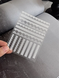Detail view of white lace nail stickers with diverse geometric patterns on transparent film