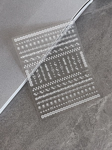 Detail of white lace nail art stickers with floral and bow patterns on stone surface