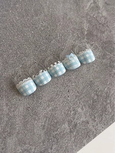 Detail of blue and white checkered press-on nails with 3D bow and lace patterns