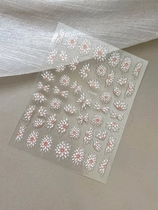 Detailed view of floral nail stickers with white and pink daisies on beige background