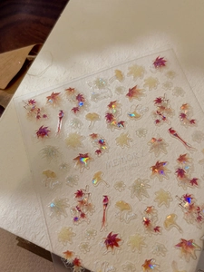 Close-up detail of holographic maple leaf nail stickers with 3D relief texture