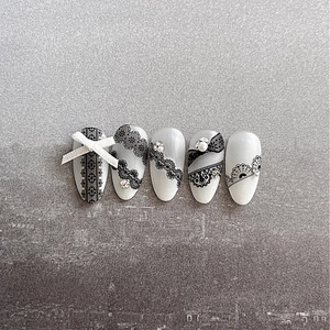 Lace french press-on nails with white bows, pearls and black patterns on grey stone