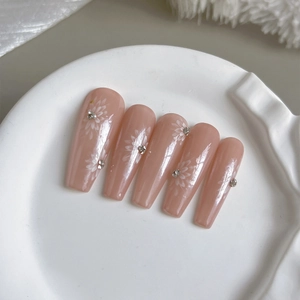 Pink press-on nails with white floral patterns and rhinestones on a ceramic dish