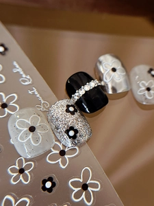 Detail of floral press-on nails with daisy patterns and rhinestone accents in black and white