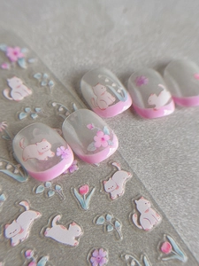 Macro shot of cute cat and pink floral nail stickers applied on French manicure nails