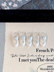 Detail of press-on nails with laser butterfly decals and white French tips on canvas