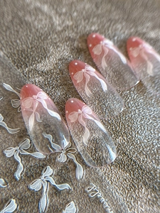 Macro detail of almond press-on nails with pink gradient and white bow design