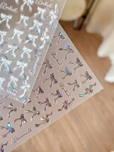 Detail of adhesive bowknot nail art stickers featuring white and iridescent laser shell finish