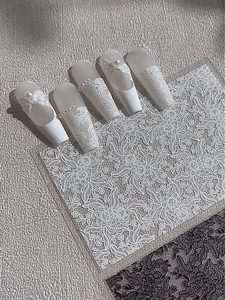 Detalle de uñas postizas de encaje blanco con lazos 3D y perlas sobre base mate