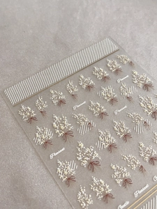Détail macro de stickers ongles fleurs blanches gaufrées avec nœuds bruns et dos adhésif