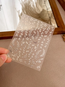 Close-up of silver leaf and flower nail stickers with metallic vine patterns and glue