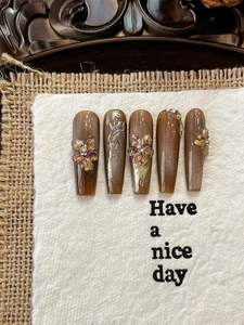 Detail of amber and dark brown cat-eye press-on nails with 3D floral and gold leaf design