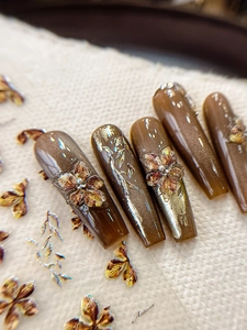 Macro shot of long coffin press-on nails with brown cat-eye effect and 3D floral accents