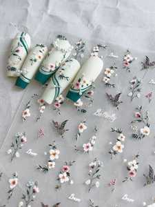 Détail d'autocollants pour ongles avec fleurs blanches, feuilles vertes et papillons