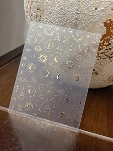 Detail of gold foil celestial nail stickers with moon and star patterns on dark wood