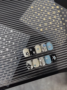 Detail view of gold and silver star nail stickers showing complex patterns on manicured nails