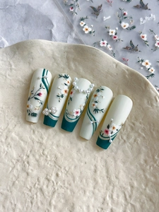 Détail de faux ongles trapèze longs avec motifs floraux mats et perles sur céramique