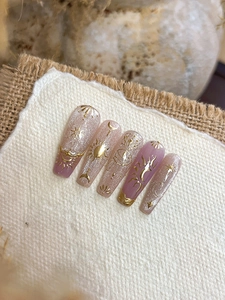 Detailed close-up of long coffin fake nails with golden celestial motifs and cat eye finish