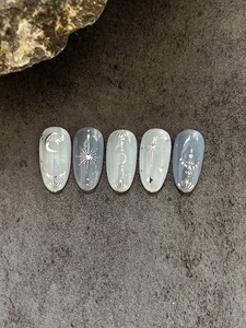 Detail of star and moon press-on nails with blue marble texture and silver glitter accents