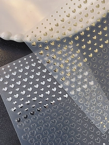 Detailed view of gold and silver heart-shaped 3D embossed nail art stickers on a white plate