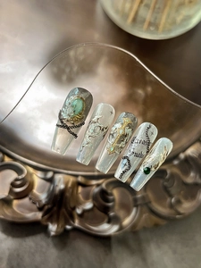 Gothic-Nagelkunst-Detail mit silbernen Schlangen, Kreuzen und grünen Edelsteinen auf Grau