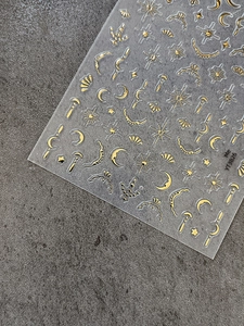 Macro shot of gold foil moon and star nail stickers with fine geometric detail on dark stone