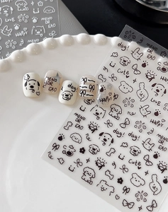 Detail of cartoon nail stickers with black dog and bow designs on creamy white fake nails