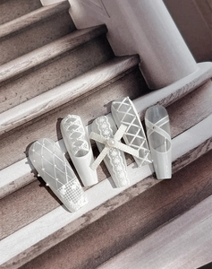 Close-up of ballet style press-on nails with lace patterns, pearls and a 3D bow detail