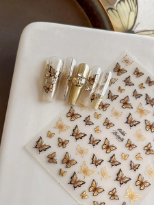 Detail view of gold butterfly nail stickers with 3D embossed texture and French style tips