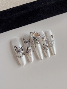Macro detail of pearly white butterfly nail tips with floral art and diamond rhinestones
