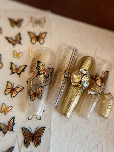 Macro detail of gold butterfly nail art with 3D rhinestones and metallic foil texture