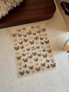 Detailed close-up of golden and black butterfly nail art stickers with embossed textures