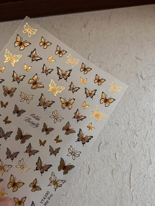 Detail of embossed golden butterfly nail stickers with intricate black hollow patterns