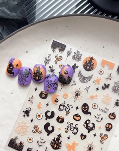 Detail of Halloween nail stickers with pumpkins and ghosts on purple sample nails