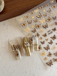 Detailed view of gold butterfly nail decals with 3D embossed texture and glitter finish
